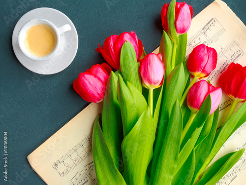 Red and white tulips on a book with music piece of music and a cup of coffee on a blue background close-up view from above