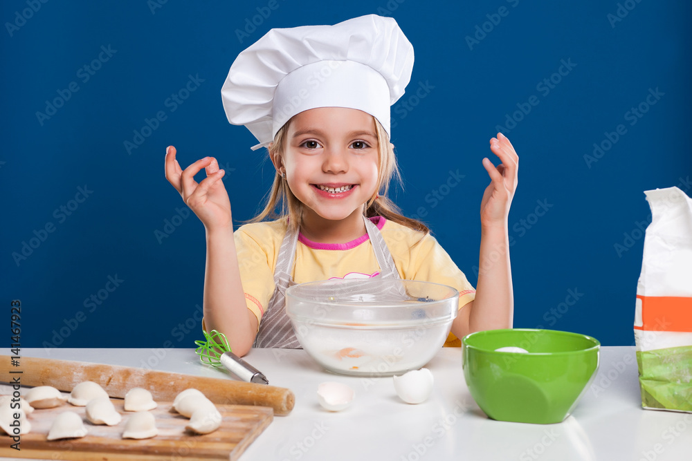 The little girl is cooking and preparing food on blue background The little girl is cooking and preparing food on blue background