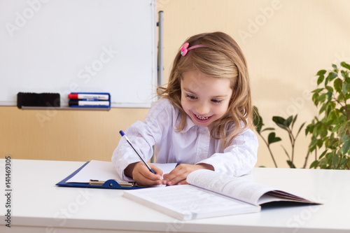 Beautiful little girl writes sitting at table