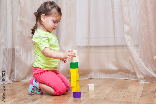 Cute little child girl sitting on the floor and playing with building blocks