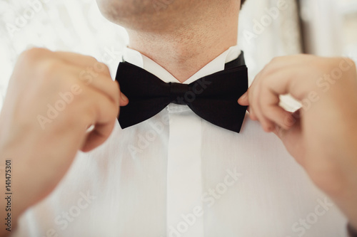 Man fixes black bow tie on his neck