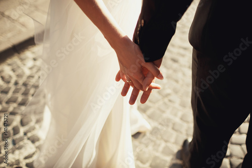 Close-up of newlyweds hands held together in the lights of evening sun