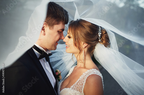 Wind blows veil on bride and groom looking at each other with love
