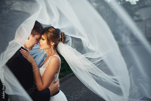 Wind blows veil on bride and groom looking at each other with love