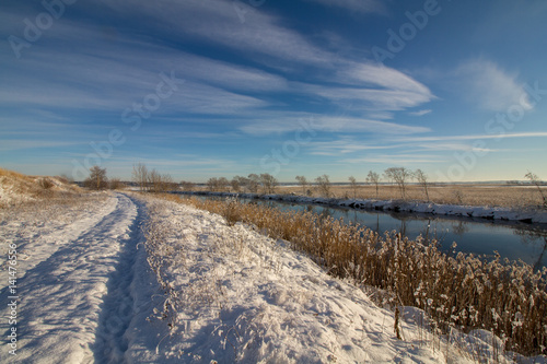 Winter landscape with snow, river, common reed, blue sky, road , sunshine. Norway