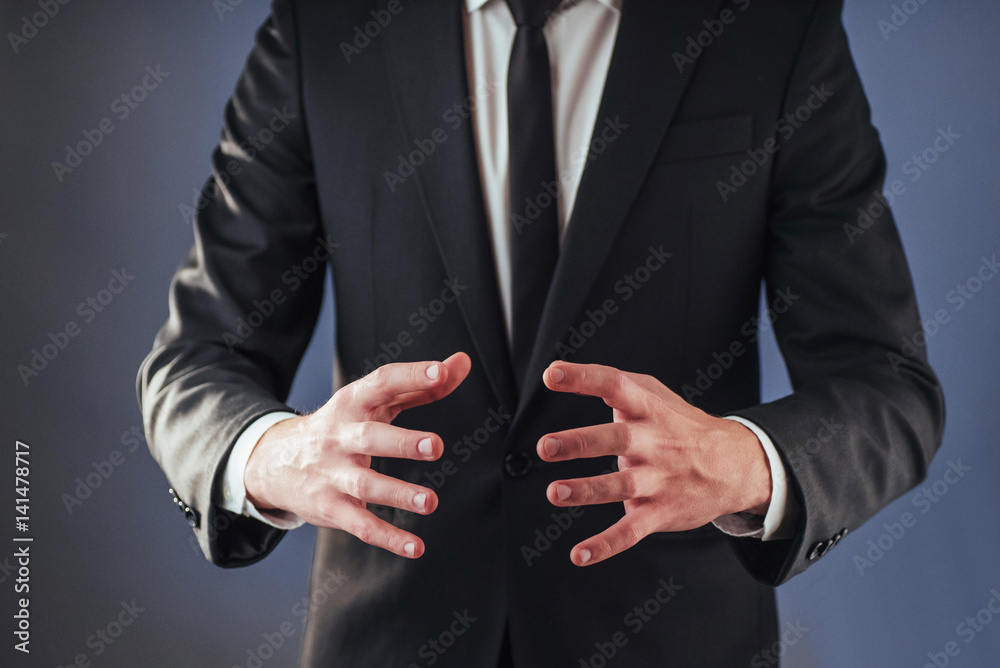Obraz premium The young businessman in a suit shows his hand on a dark background isolated