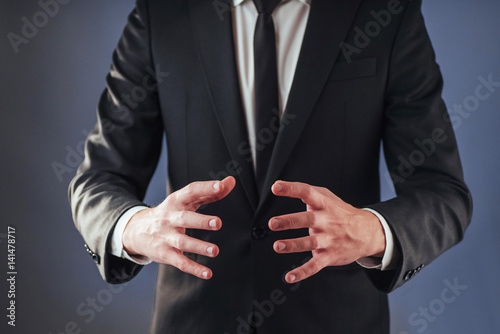 The young businessman in a suit shows his hand on a dark background isolated