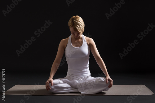 Woman exercising yoga indoor on black background,Lotus position/Padmasana