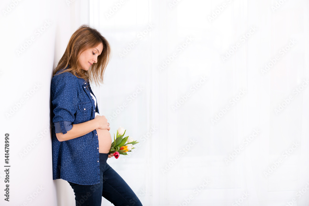 Young pregnant woman, holding tulip flowers, leaning on a wall Young pregnant woman, holding tulip flowers, leaning on a wall