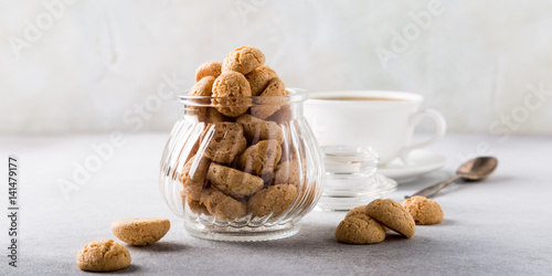 Amaretti cookies in glass pot with white cup of coffee on light gray background with copy space.