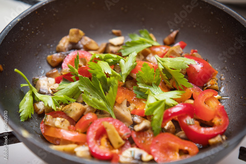 Mushrooms and fresh sweet red pepper in the pan for cooking. Spices and fresh parsley. Shallow depth of field. Toned