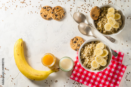 Healthy breakfast. Light background with red napkin. Barley porridge, flax seeds, bananas, soy milk, peach juice and cookies with chocolate chips.