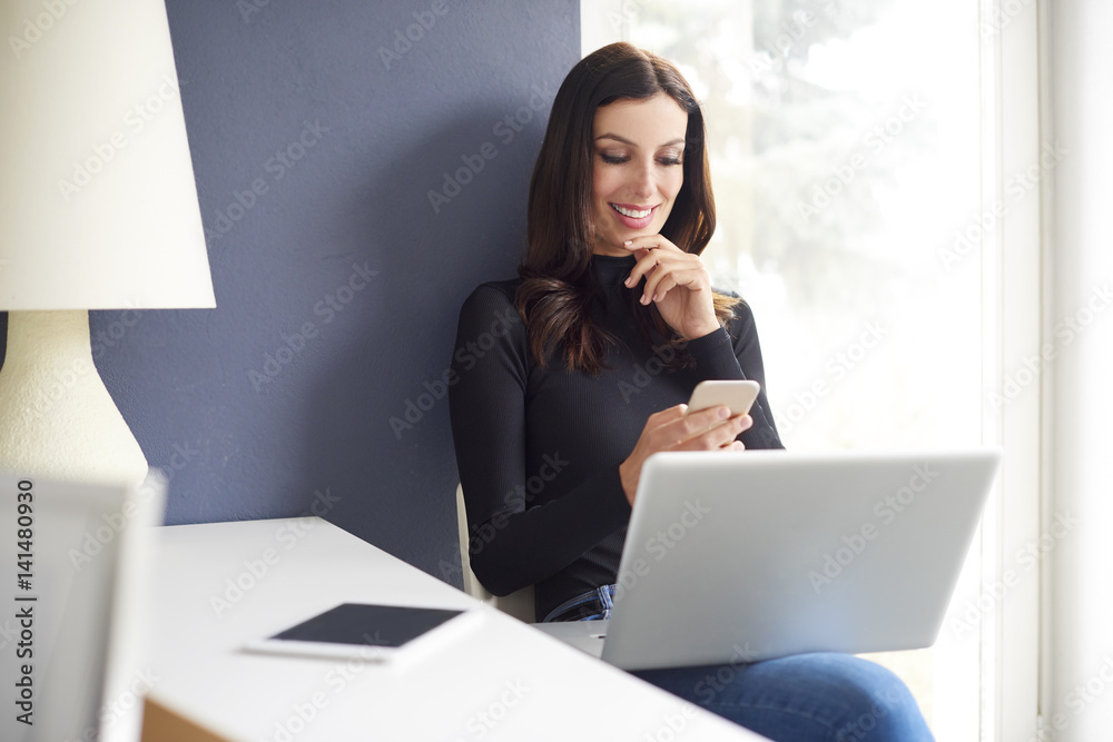 Getting good news. Shot of a happy businesswoman reading text message on her cellphone while sitting in front of laptop at office. Getting good news. Shot of a happy businesswoman reading text message on her cellphone while sitting in front of laptop at office.