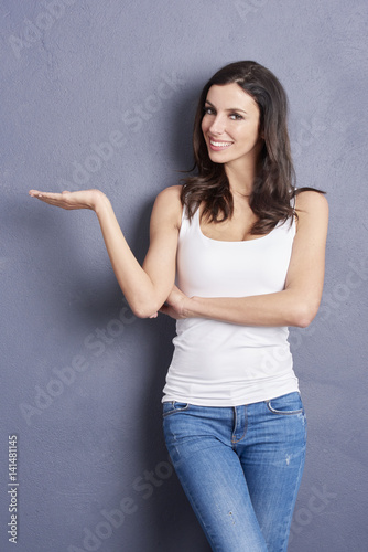 Young beautiful woman pointing at copy space while looking at camera and smiling.