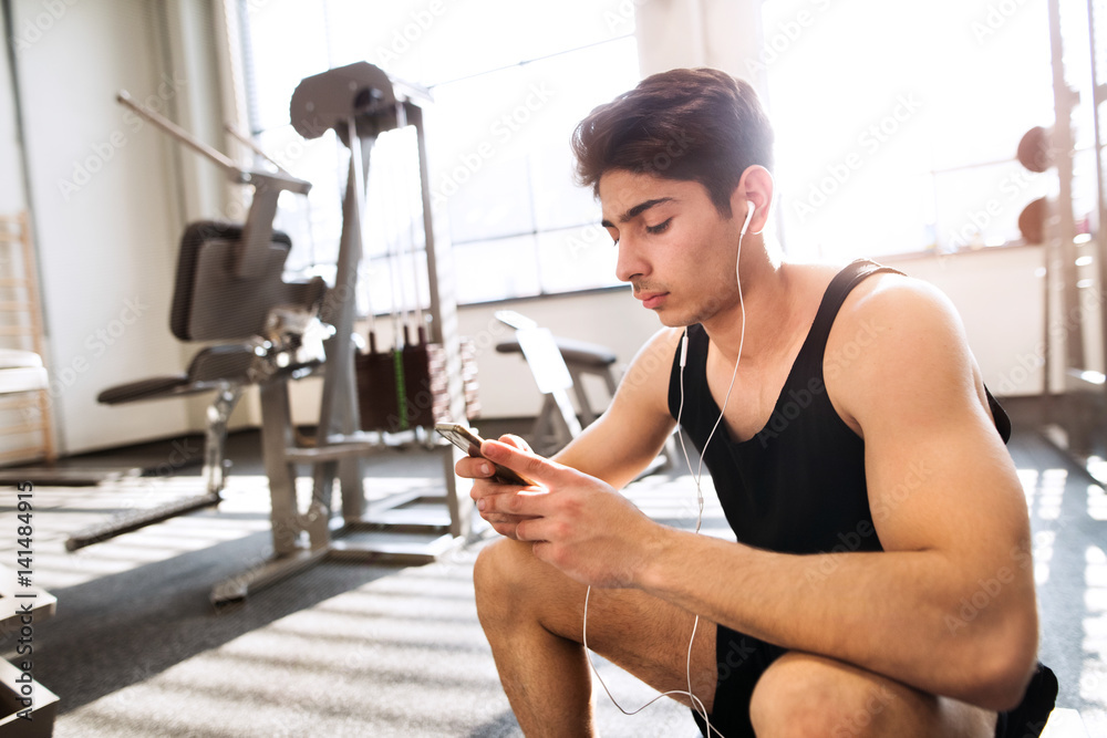Hispanic man in gym resting, holding smart phone, listening musi Hispanic man in gym resting, holding smart phone, listening musi