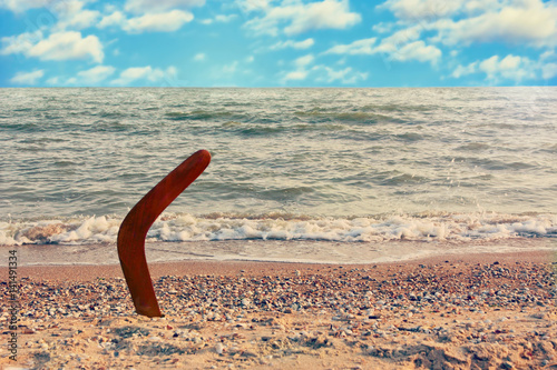 Australian Boomerang on sandy coastline against sea wave and sky.Toned image.
