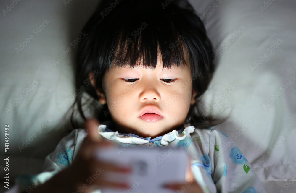 Cute little girl in pajamas playing smartphone lying on a bed Cute little girl in pajamas playing smartphone lying on a bed