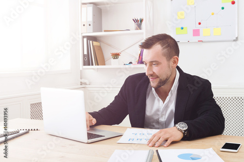 Young businessman working with laptop in modern white office