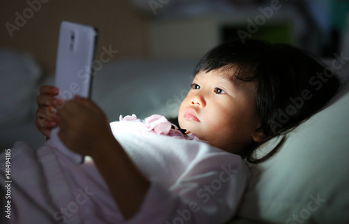 Kid girl playing smartphone lying on a bed at night