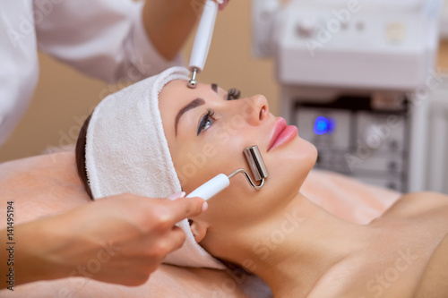 The physician-cosmetologist makes the apparatus a procedure of  galvanic  ultrasound cleaning of the face skin of a beautiful  young woman in a beauty salon. Cosmetology and professional skin care.