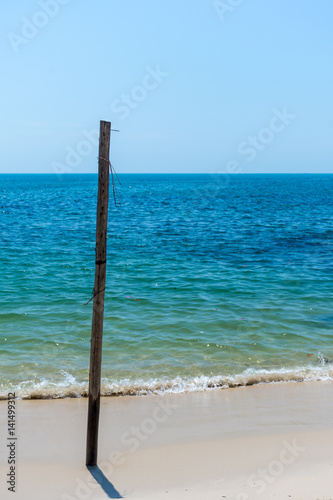 Old Wooden post stuck in white sandy beach.