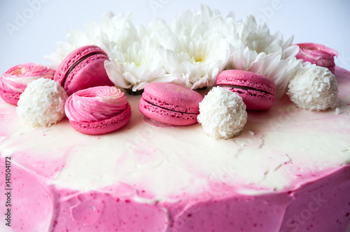Wedding cake with white spring flowers and macaroon on top. Delicious pink cake isolated on white background.
