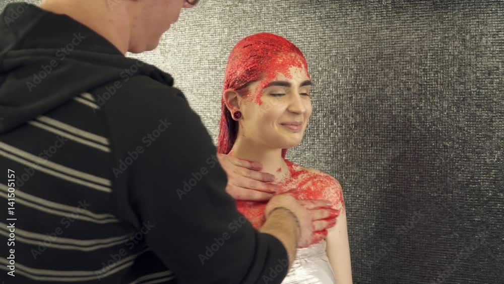 Makeup artist covering girl's body with red paint Makeup artist covering girl's body with red paint