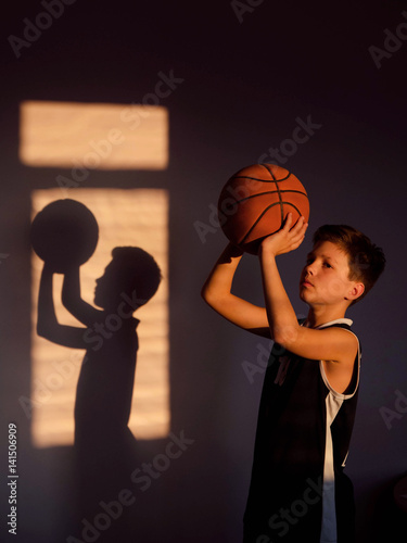 A boy throws a basketball. Shadow on the wall basketball player at sunset photo