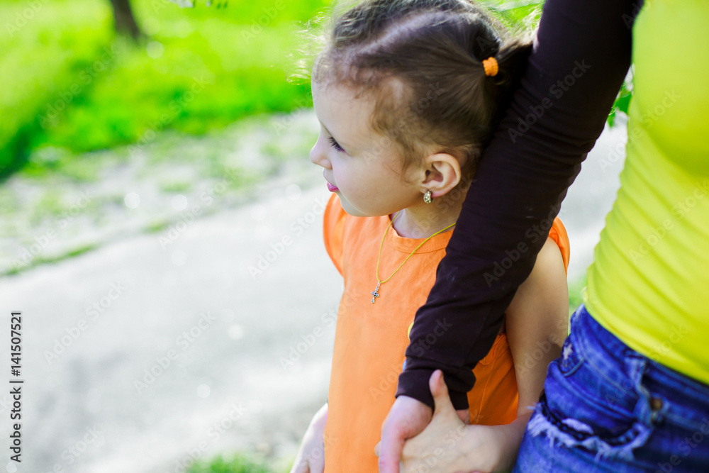 The girl walks along the road holding her mother's hand. Mom leads a child in the street. Walking in the fresh air in the spring. The girl walks along the road holding her mother's hand. Mom leads a child in the street. Walking in the fresh air in the spring.
