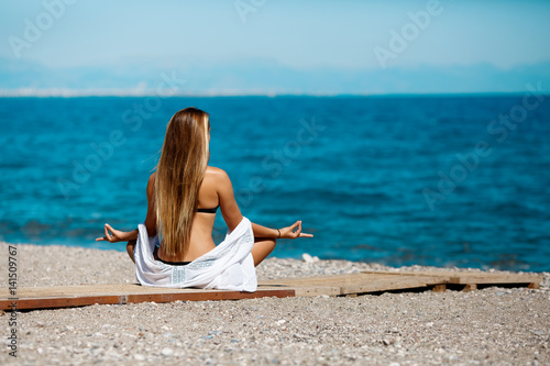 Sports yoga girl doing fitness exercises and meditation at beach near pool. Fitness workout concept. Slim perfcet body yoga girl at seashore makes asana. photo