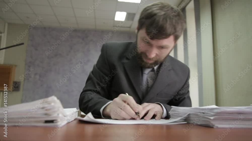 Businessman nervously signing and stamping incoming documents. office worker shifts papers from one pile to another Businessman nervously signing and stamping incoming documents. office worker shifts papers from one pile to another