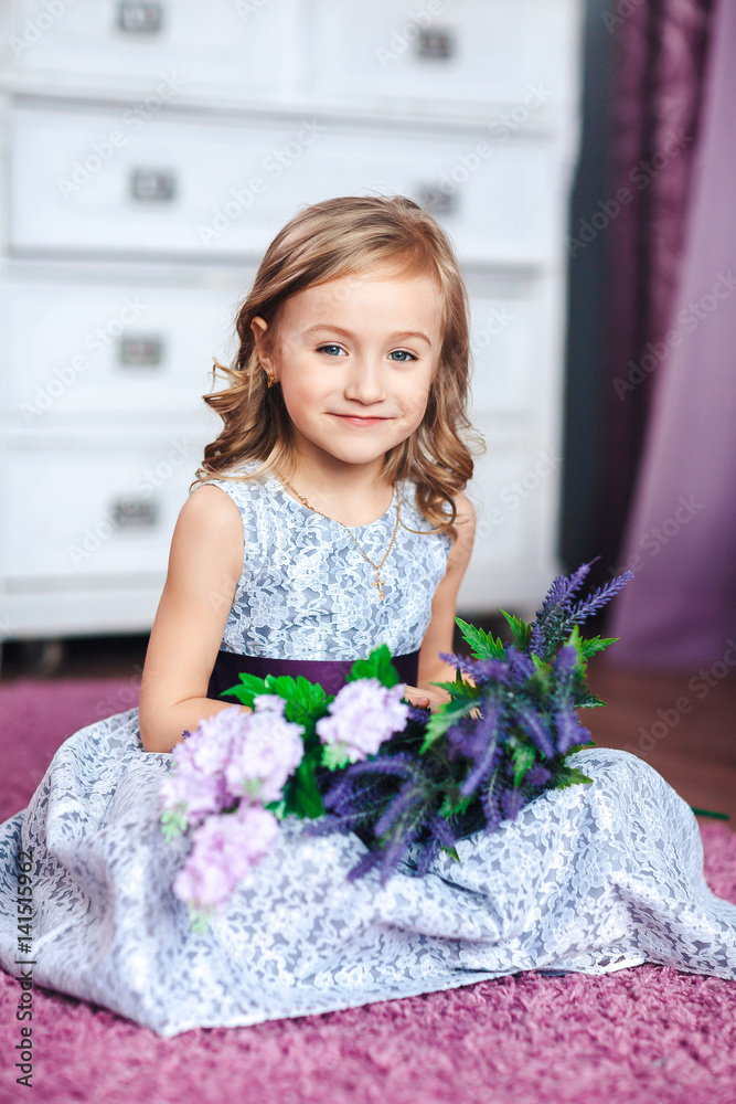 Little blonde girl in a beautiful dress sits on the floor with flowers on her knees Little blonde girl in a beautiful dress sits on the floor with flowers on her knees