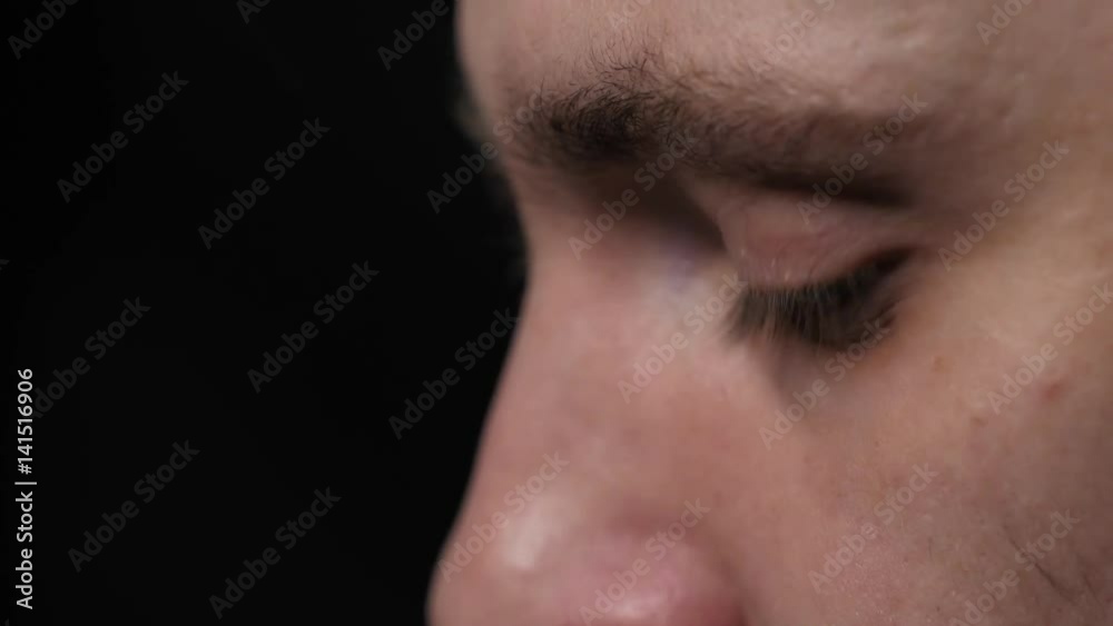 Young handsome man putting contact lens in his blue eye close up isolated on black background.