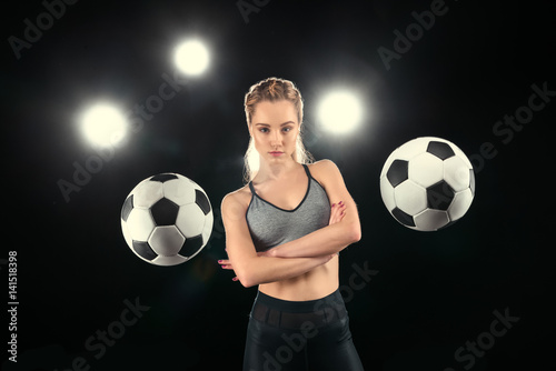Confident young sportswoman with crossed arms posing between soccer balls © LIGHTFIELD STUDIOS