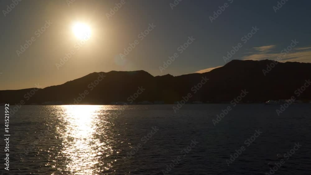 Reflection of the sun in the sea. You can see the silhouettes of mountains and boats Reflection of the sun in the sea. You can see the silhouettes of mountains and boats
