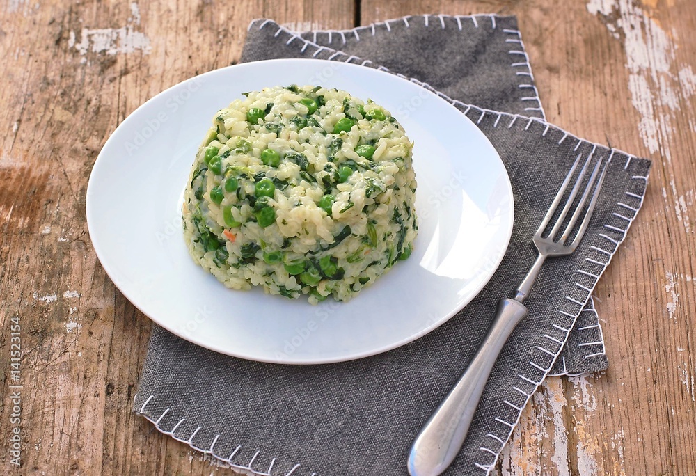 Creamy risotto with peas and spinach on white plate on grey cloth on rustic table Creamy risotto with peas and spinach on white plate on grey cloth on rustic table