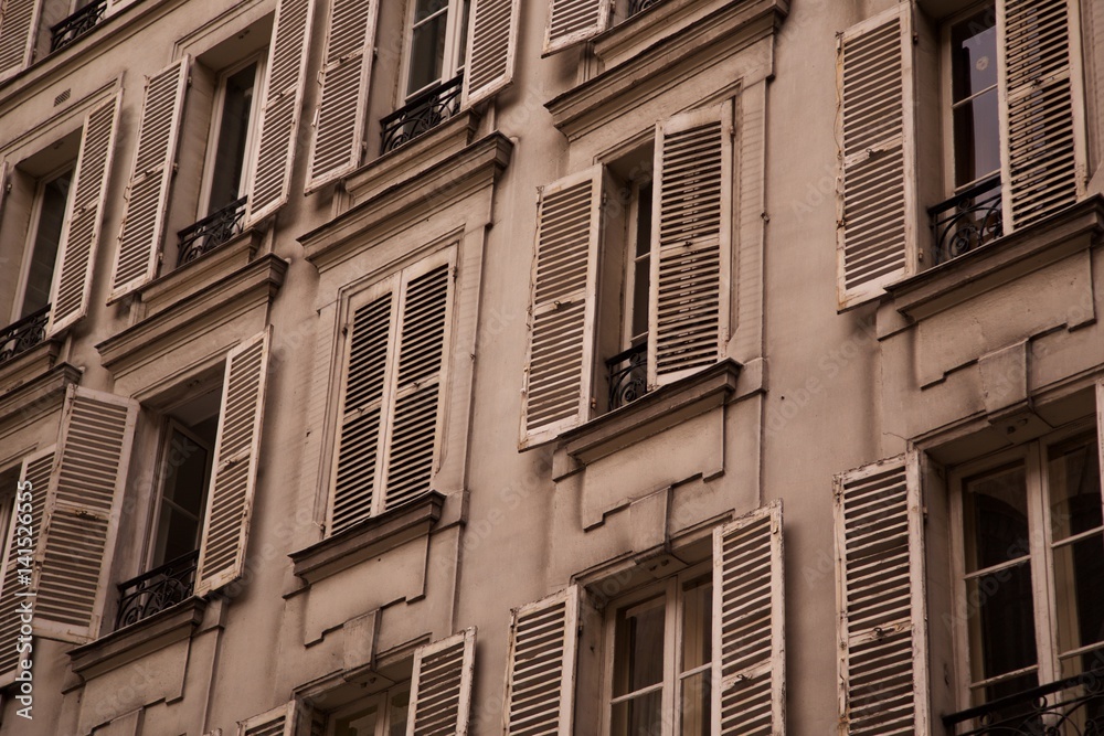 Obraz premium Low perspective of old dirty weathered vintage stucco apartment building exterior with rows of open and shut old fashion wood shutter window balcony in historic Europe