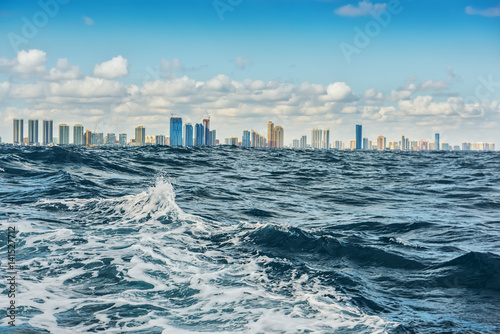 View of the city on the coast from the sea. The stormy elements of the waves, skyscrapers on the horizon and a beautiful sky in the clouds. USA. Miami, the Atlantic Ocean. 