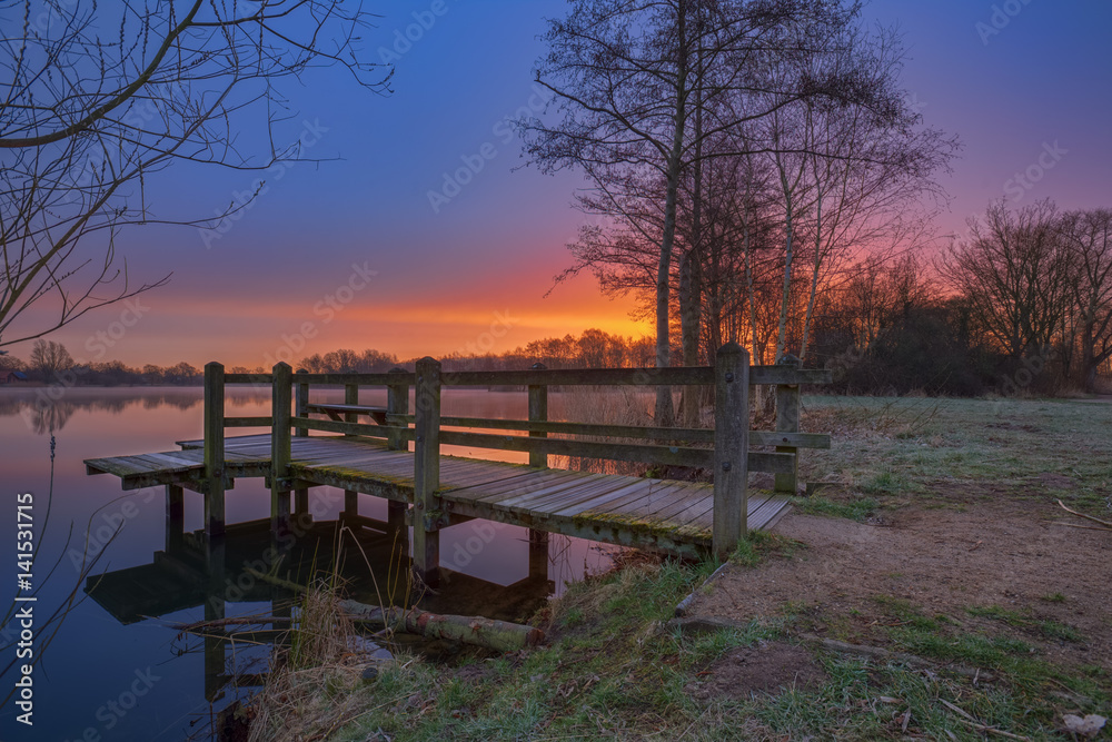 Fototapeta premium Morgens am Steg / Sonnenaufgang über dem Thielenburger See in Dannenberg (Landkreis Lüchow - Dannenberg, Niedersachsen, Deutschland). Aufgenommen am 19. März 2017.