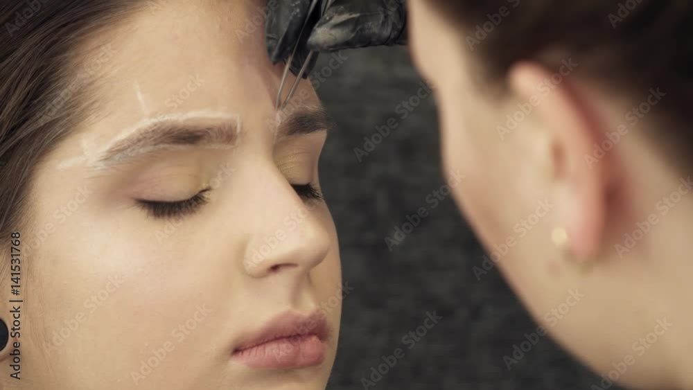 Beautician artist fixing the shape of eyebrows for a woman Beautician artist fixing the shape of eyebrows for a woman