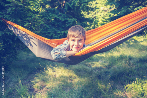 Cute smiling boy is swinging in a hammock in a forest glade