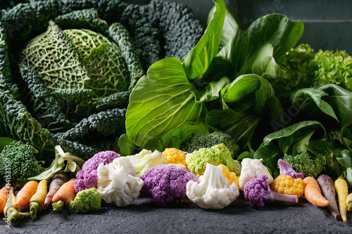 Variety of raw green vegetables salads  lettuce  bok choy  corn  broccoli  savoy cabbage  colorful young cauliflower over black stone texture background. Close up