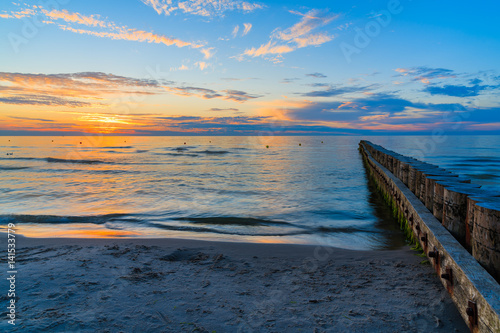 Sunset over sea with wooden breakwaters in foreground on Leba beach, Baltic Sea, Poland