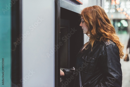 Young beautiful caucasain woman at night withdrawing money from atm - withdrawal, money concept photo