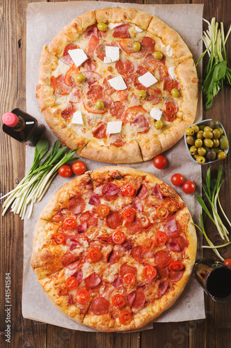 Rustic pizza with salami, mozzarellabasil top view with copy space. Two pizzas on a wooden table. Pizza salami on wooden background. Pizza salami with tomatoes and olives