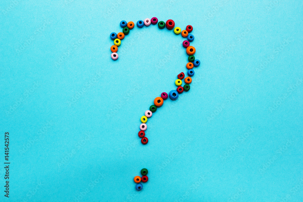 Multi-colored children's beads, scattered on a blue background, question mark. Multi-colored children's beads, scattered on a blue background, question mark.