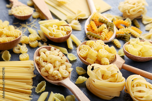 Different kinds of pasta in wooden spoon on grey table