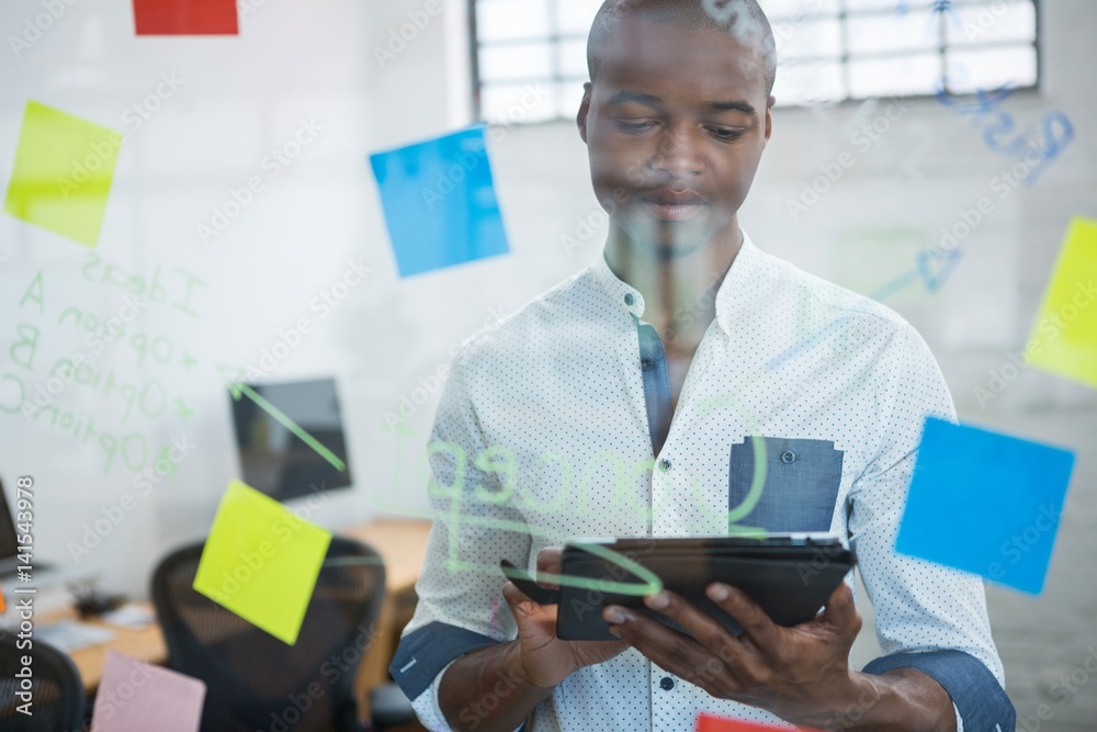 Businessman using digital tablet while writing on sticky note Businessman using digital tablet while writing on sticky note