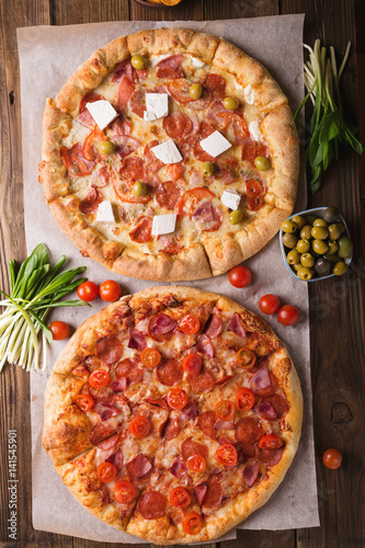 Rustic pizza with salami, mozzarellabasil top view with copy space. Two pizzas on a wooden table. Pizza salami on wooden background. Pizza salami with tomatoes and olives