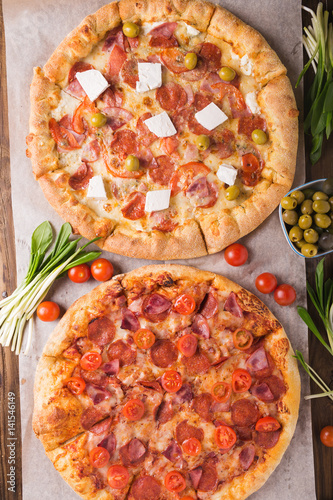 Rustic pizza with salami, mozzarellabasil top view with copy space. Two pizzas on a wooden table. Pizza salami on wooden background. Pizza salami with tomatoes and olives